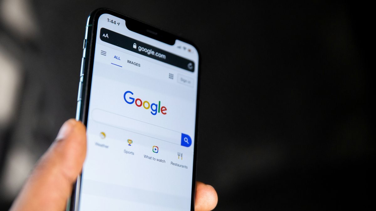 Pessoa segurando um celular com a página de busca do Google aberta, em um ambiente escuro.