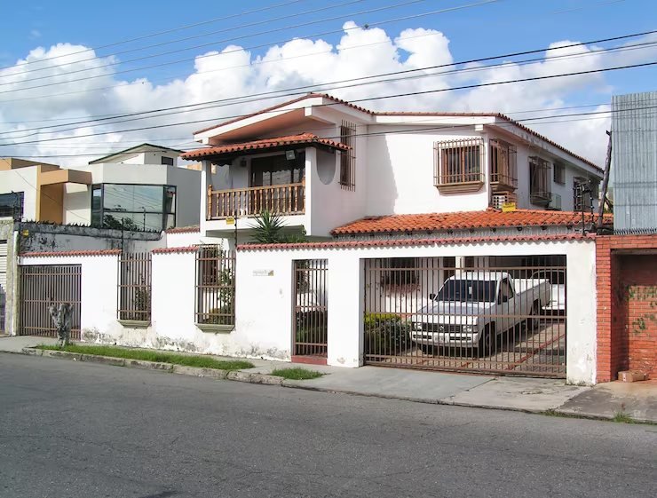 Rua residencial com casas de fachadas claras e telhado de telha, em um dia de céu limpo.